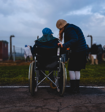 Side image, consisting of a woman attending an elderly man on a wheelchair.